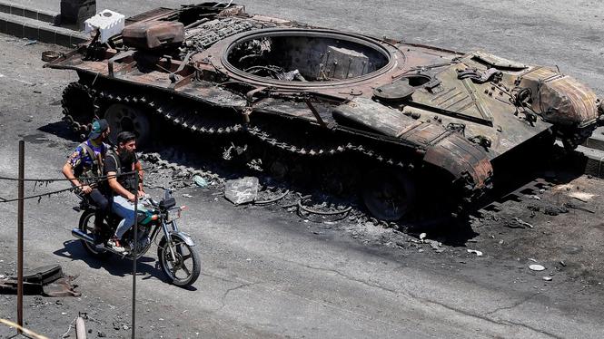 Två drusiska milismän passerar en utbrunnen stridsvagn i Suweida, där omkring 100 drusiska kvinnor nu saknas efter de sekteristiska striderna mellan druser och beduiner.