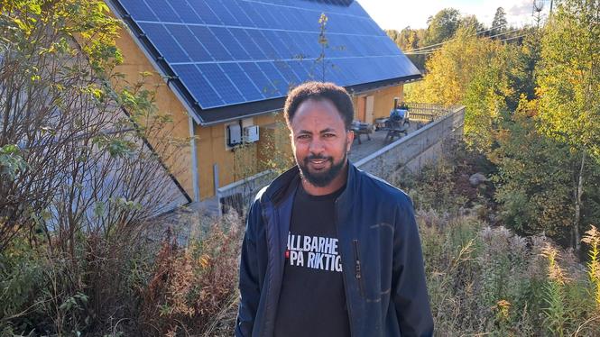 Bakom solcellsmontör Abraham Tesfaldet syns baksidan av cafébyggnaden Solhuset, där återbrukade solpaneler används till takets norra sida.