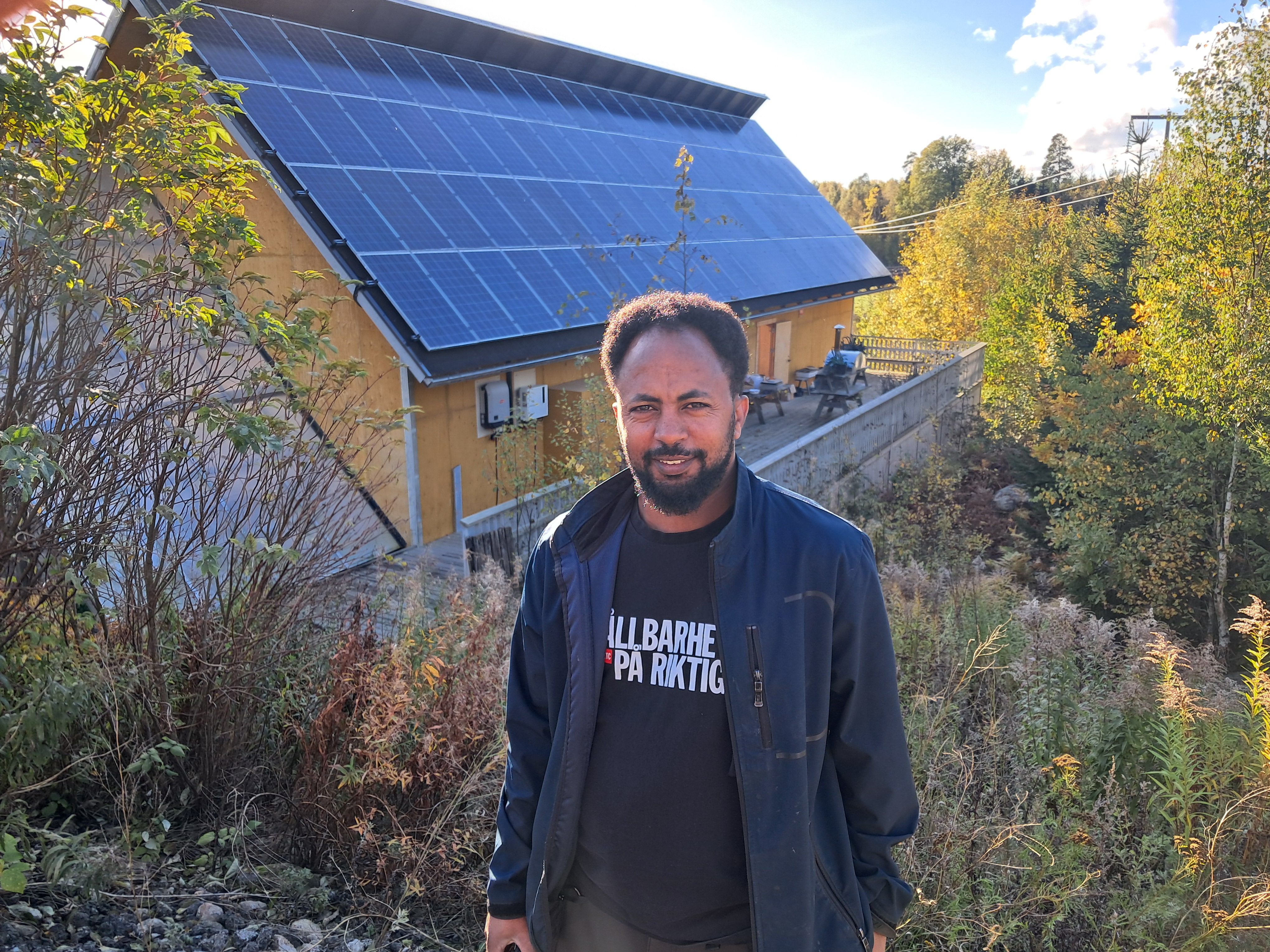 Bakom solcellsmontör Abraham Tesfaldet syns baksidan av cafébyggnaden Solhuset, där återbrukade solpaneler används till takets norra sida.