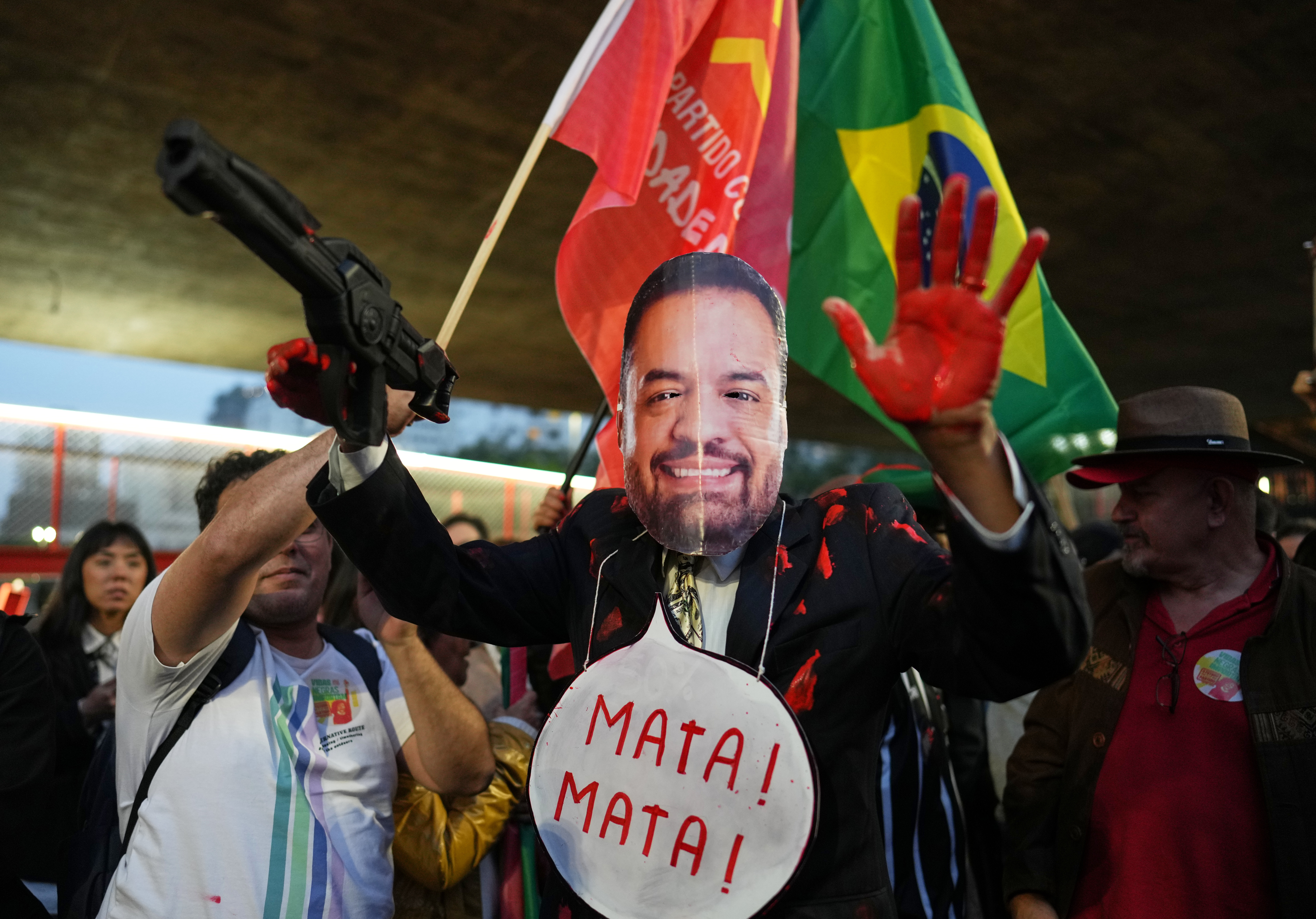 Döda! Döda! Så står det i pratbubblan som demonstranten, maskerad till Rio de Janeiros guvernör Claudio Castro, bär runt sin hals.