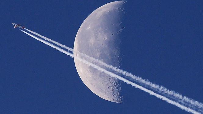 Ett flygplan lämnar ett spår på himlen när det passerar månen över Frankfurt, Tyskland.