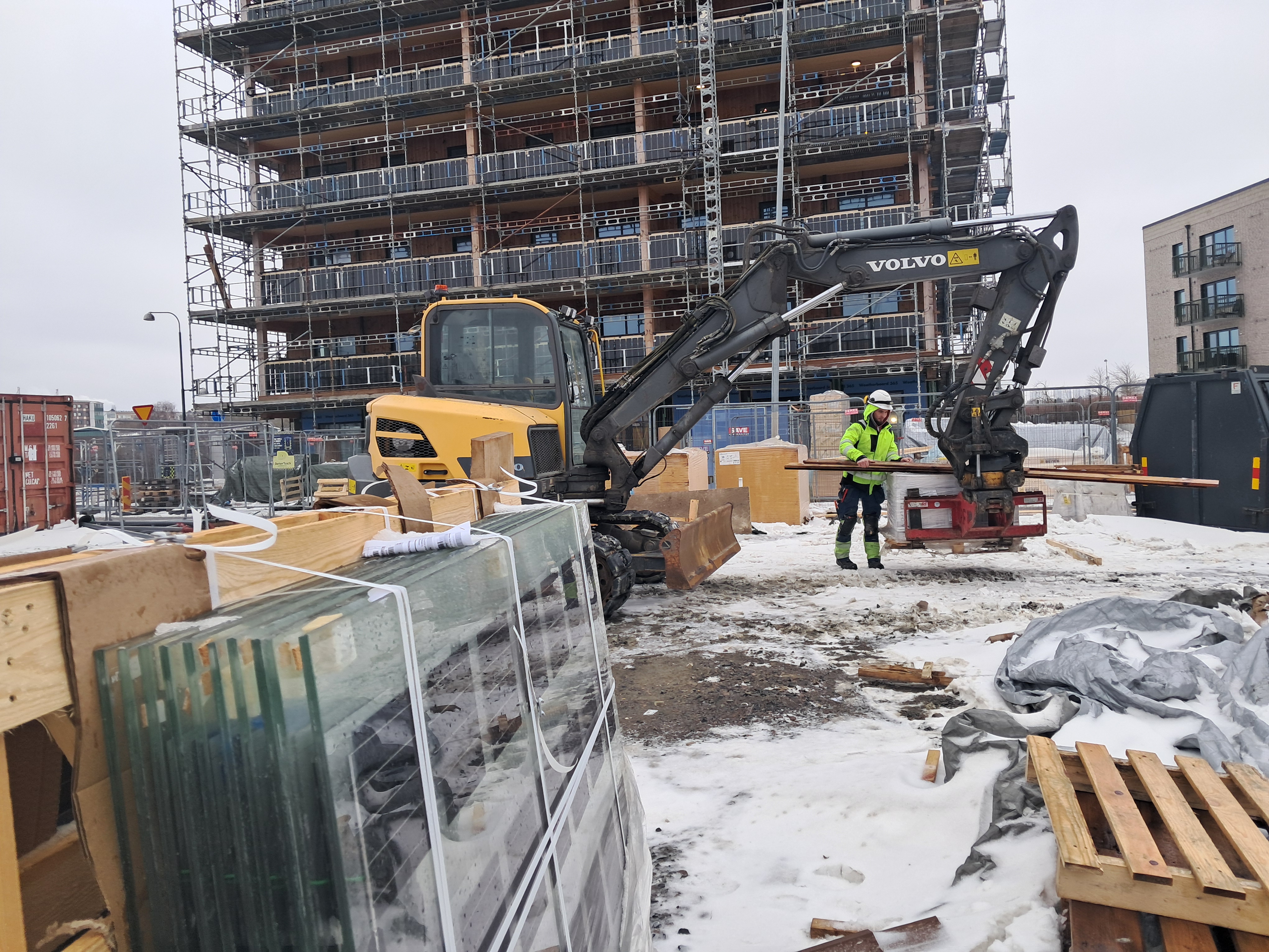 Här lastas trätrall till balkonger på husets översta våningsplan. I förgrunden syns solceller som installeras i balkongbalustraderna.