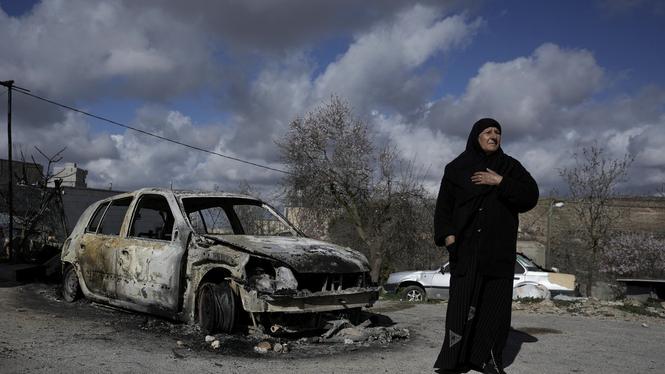 En palestinsk kvinna bredvid en utbränd bil i byn Jalud på den ockuperade Västbanken. Bild från 2023. 