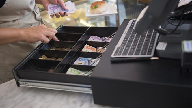 Personal hanterar kontanter i kassa i butik.