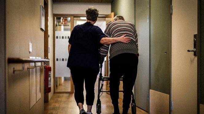 En person går med rullator med ett vårdbiträde bredvid på ett omsorgsboende för äldre. Arkivbild.
